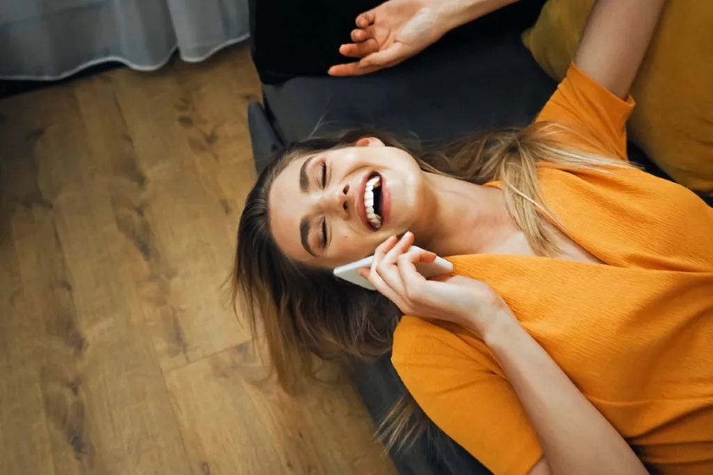 Imagem mostra uma mulher falando ao celular deitada em um sofá