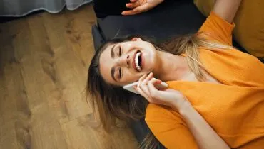 Imagem mostra uma mulher falando ao celular deitada em um sofá