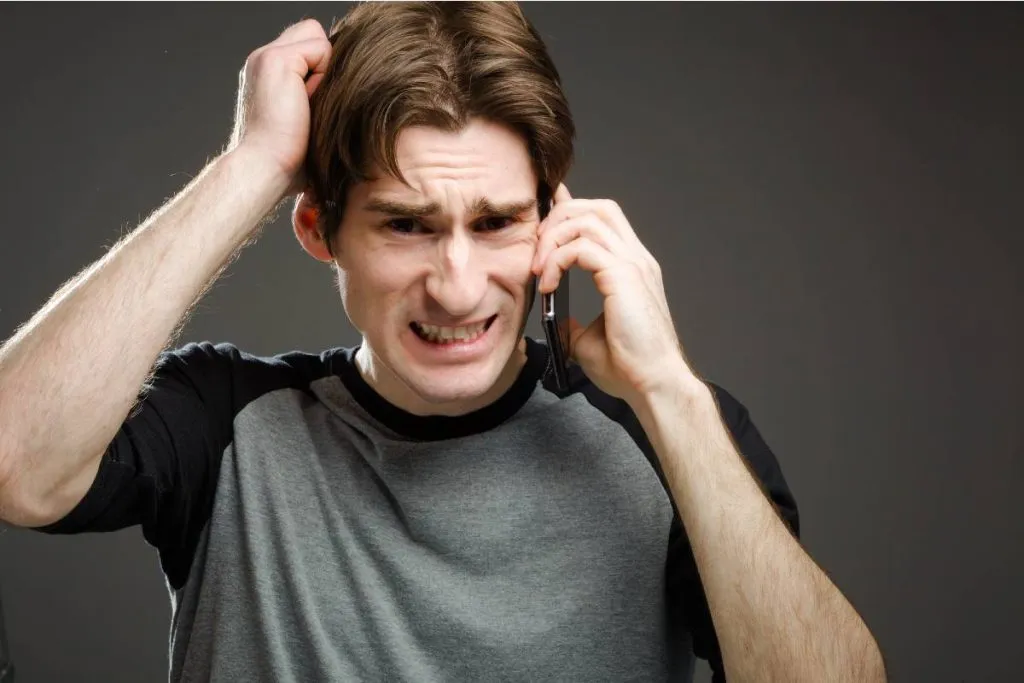 Imagem mostra um homem nervoso ao celular.