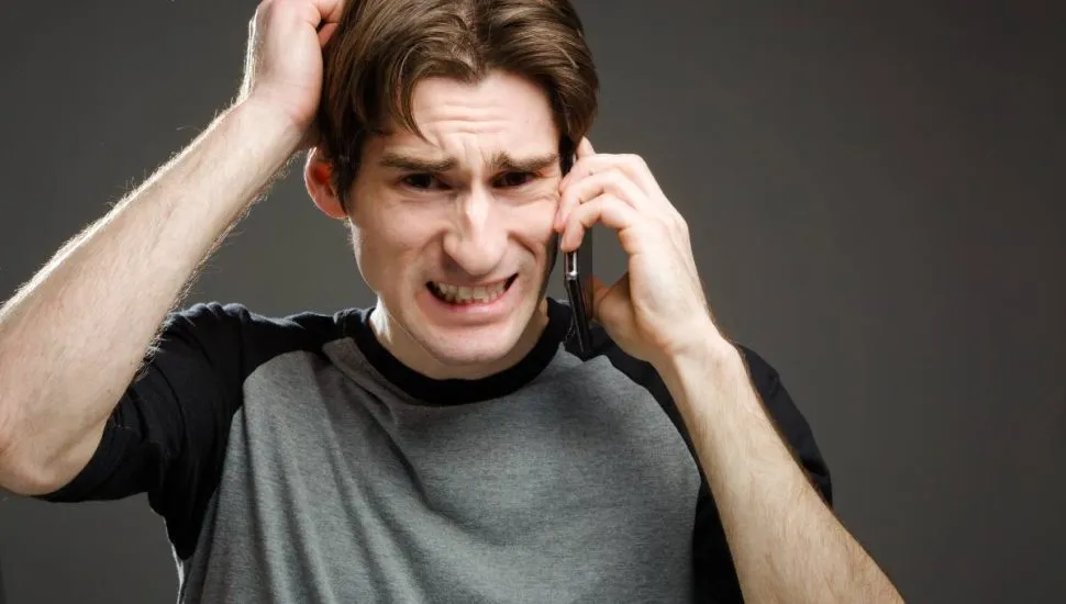 Imagem mostra um homem nervoso ao celular.