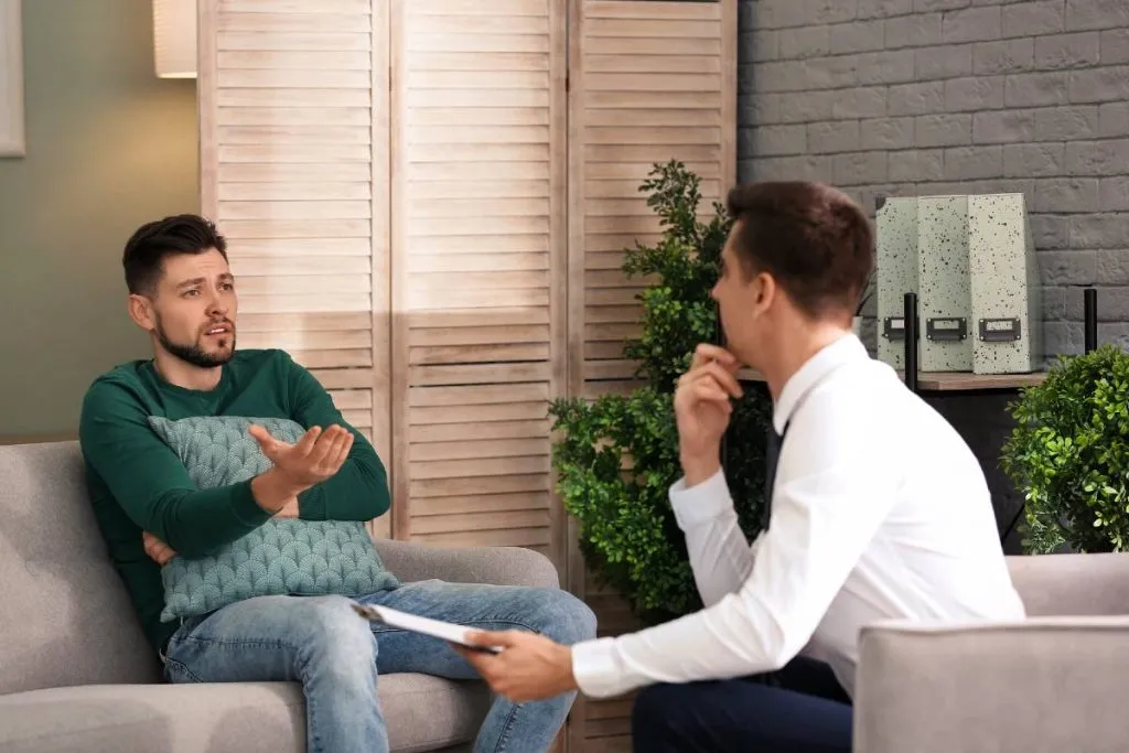 Imagem mostra duas pessoas conversando em um sofá de casa.