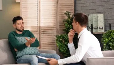 Imagem mostra duas pessoas conversando em um sofá de casa.