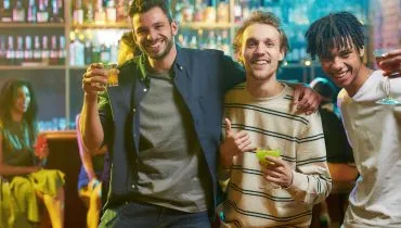 Imagem mostra três pessoas bebendo em um bar.