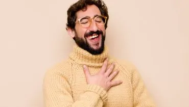 Imagem mostra um homem de blusa de lã bege rindo de forma sarcástica.