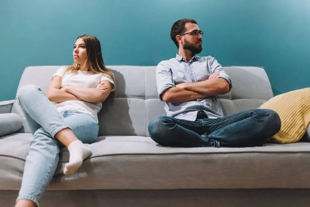 Imagem mostra um casal sentado em um sofá após uma discussão de relacionamento