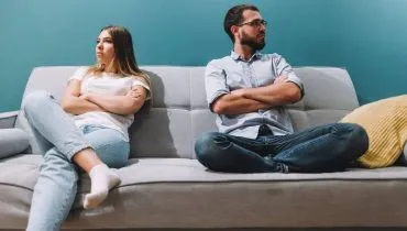 Imagem mostra um casal sentado em um sofá após uma discussão de relacionamento