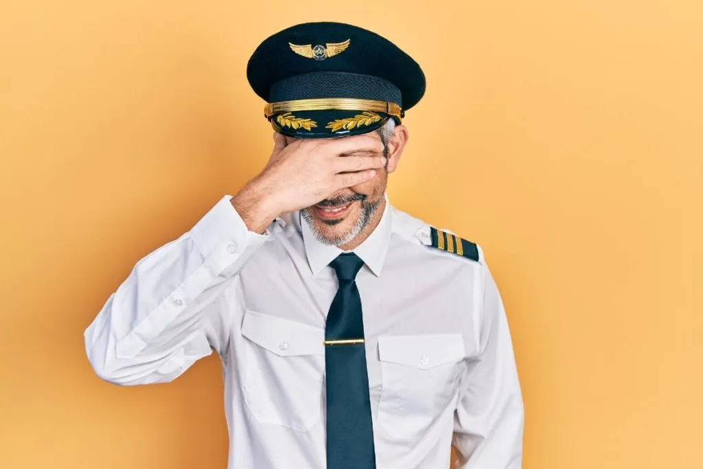 Imagem mostra um homem vestido de piloto com a mão na cabeça e rindo.