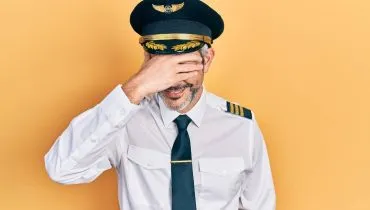 Imagem mostra um homem vestido de piloto com a mão na cabeça e rindo.