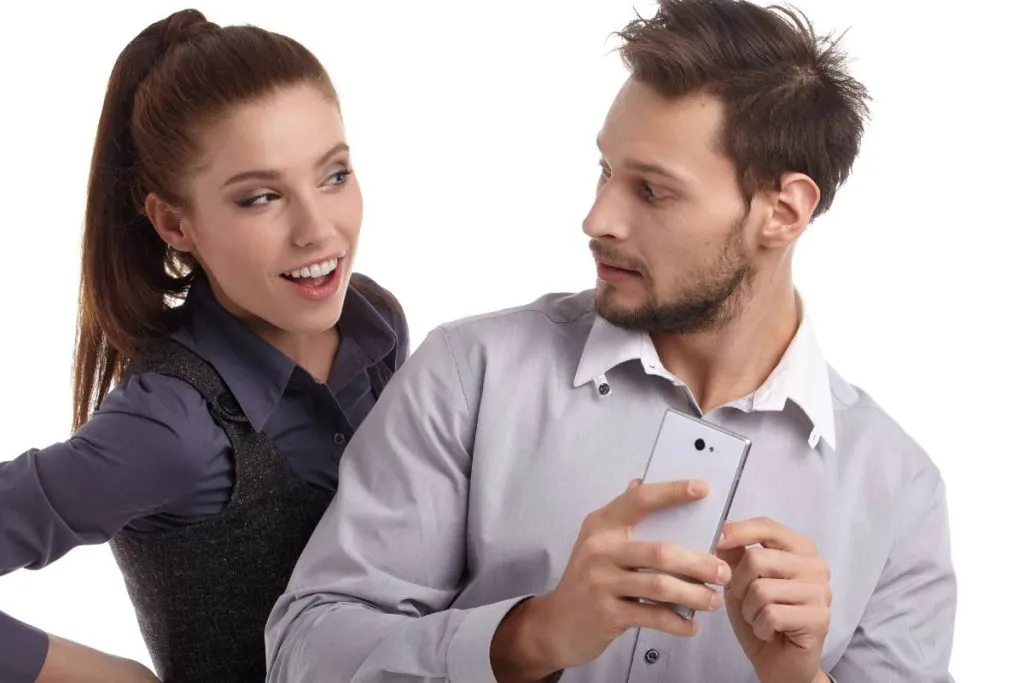 Imagem mostra um homem escondendo o celular de uma mulher que está de olho logo atrás.