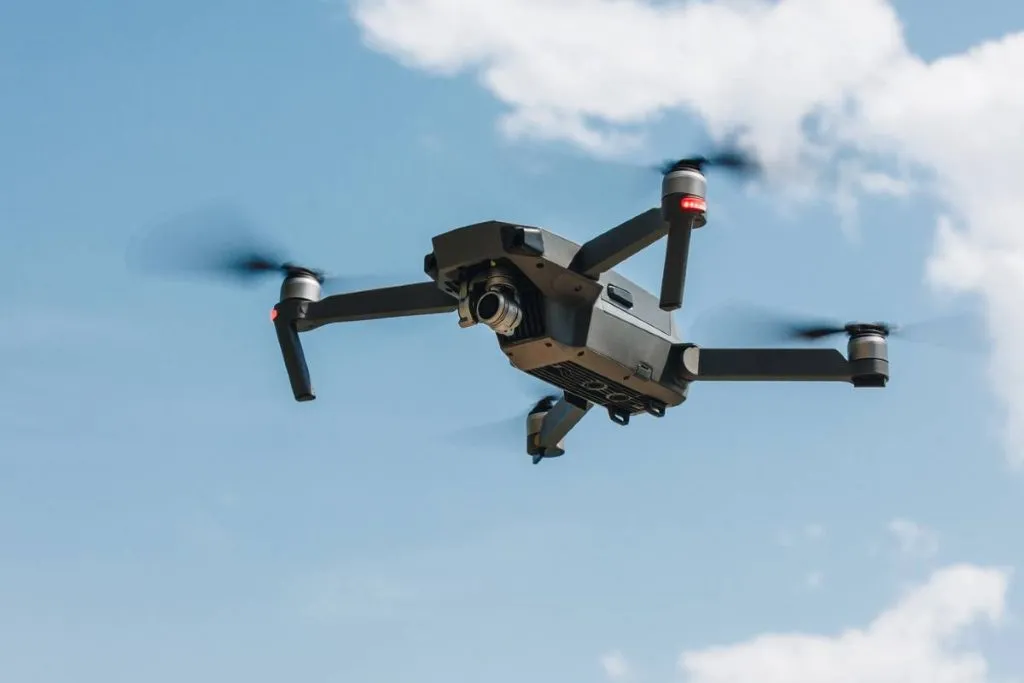 Imagem mostra um drone voando em um céu azul com uma nuvem ao fundo.