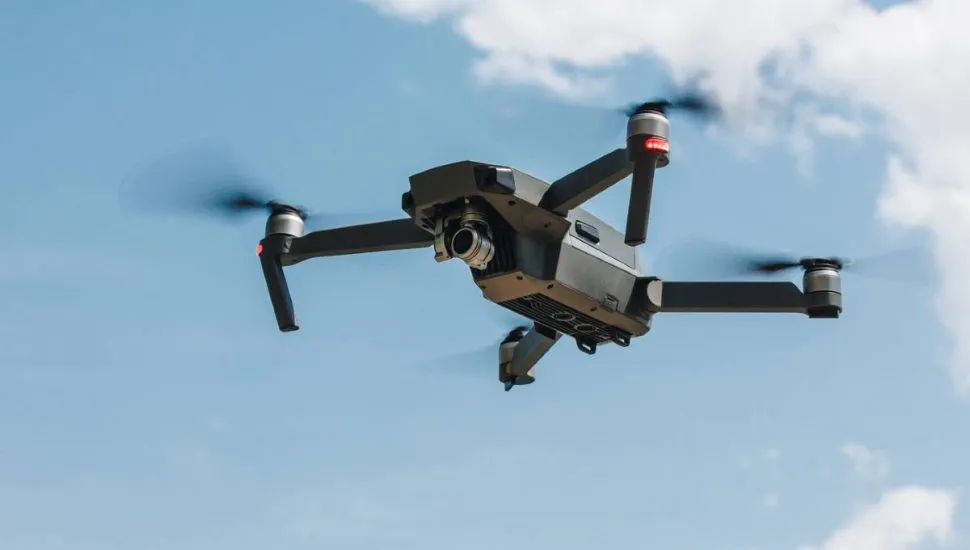 Imagem mostra um drone voando em um céu azul com uma nuvem ao fundo.