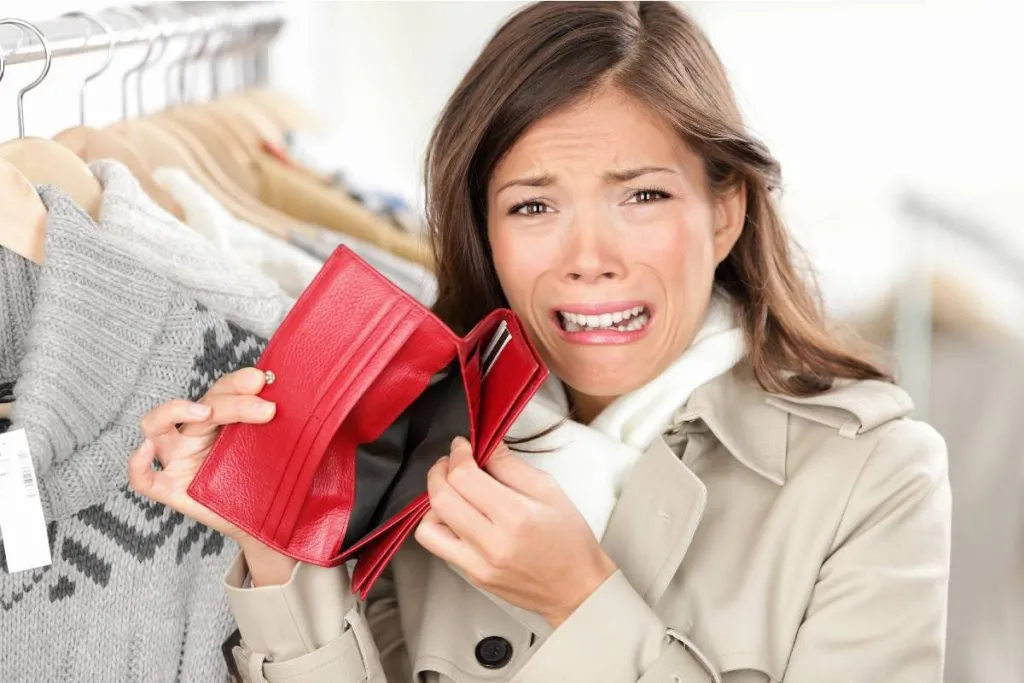 Imagem mostra uma mulher com cara de desespero abrindo uma carteira vazia, sem dinheiro.