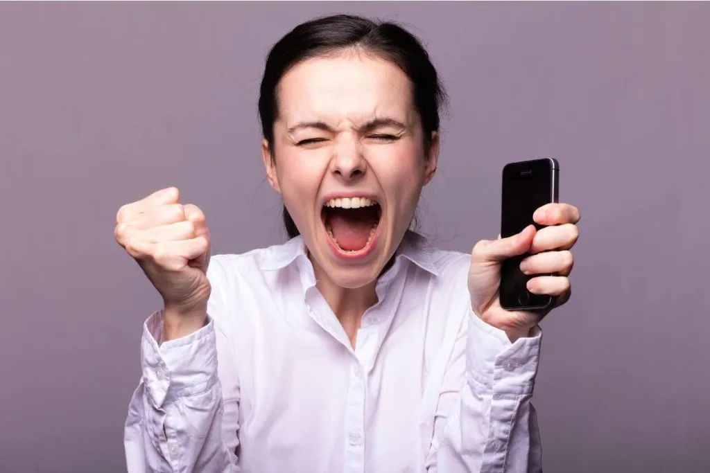 Imagem mostra uma mulher furiosa com o celular na mão.