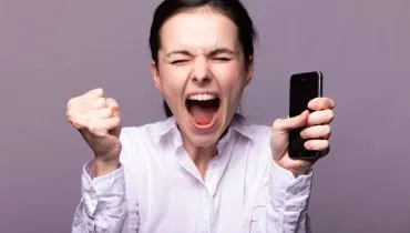 Imagem mostra uma mulher furiosa com o celular na mão.