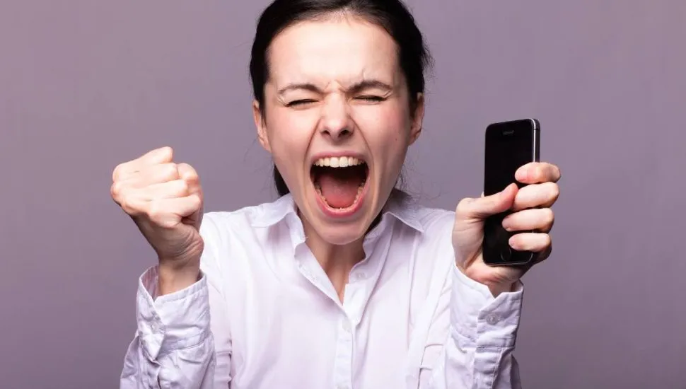 Imagem mostra uma mulher furiosa com o celular na mão.