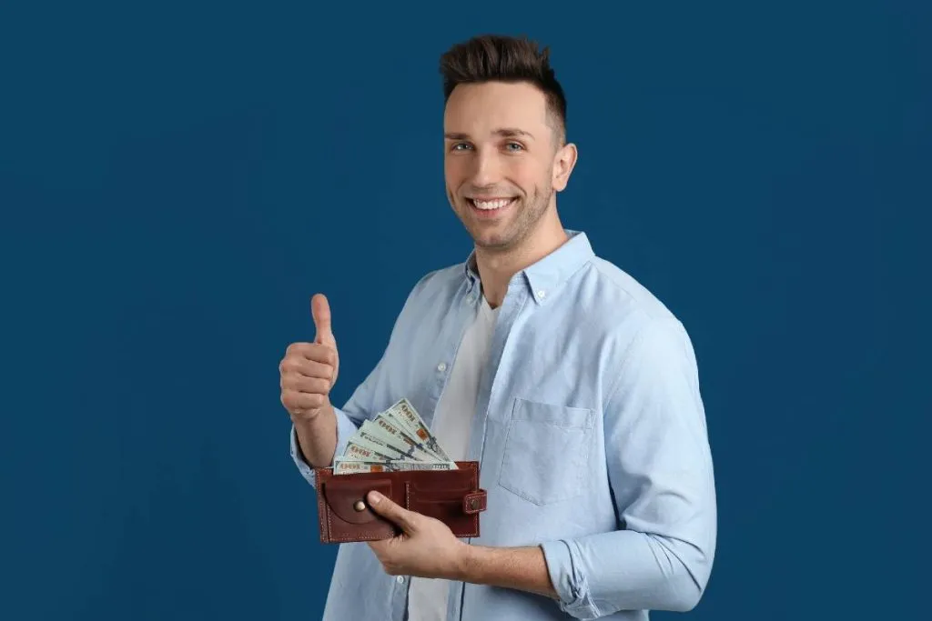 Imagem mostra um homem feliz fazendo joinha e com a carteira cheia.