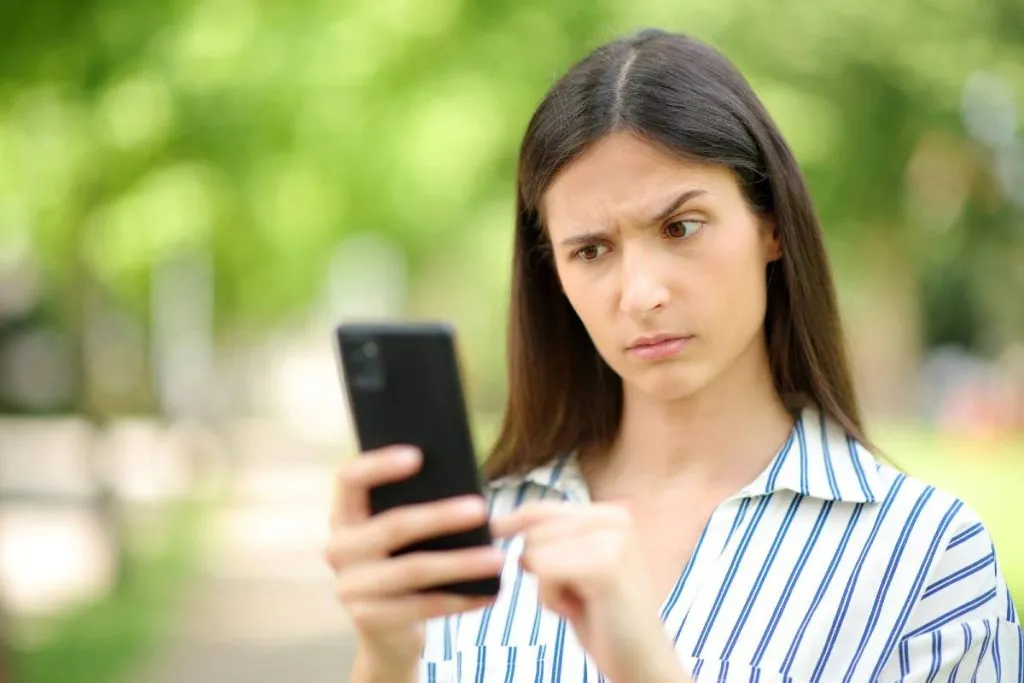 Imagem mostra uma mulher olhando um celular com cara de desconfiada.