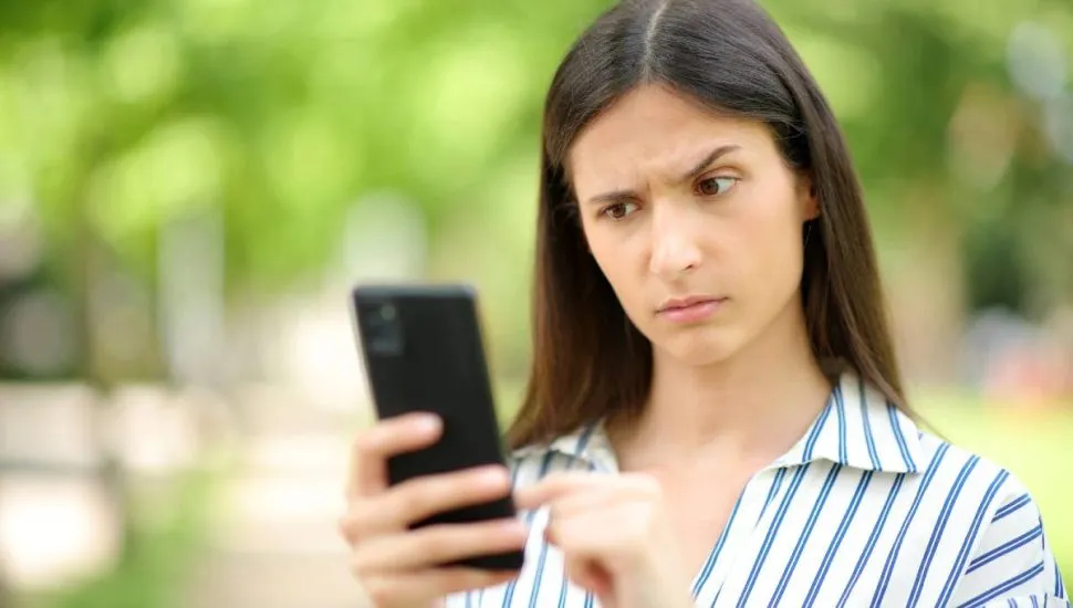 Imagem mostra uma mulher olhando um celular com cara de desconfiada.