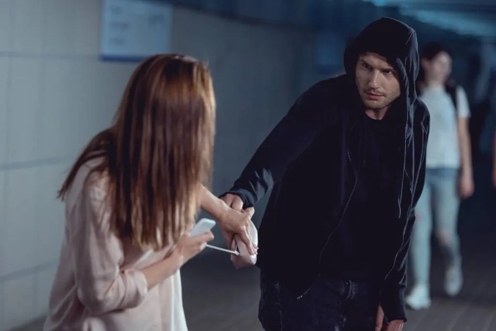 Imagem mostra uma mulher sendo assaltada por um homem de capuz.