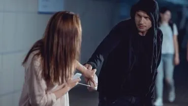 Imagem mostra uma mulher sendo assaltada por um homem de capuz.