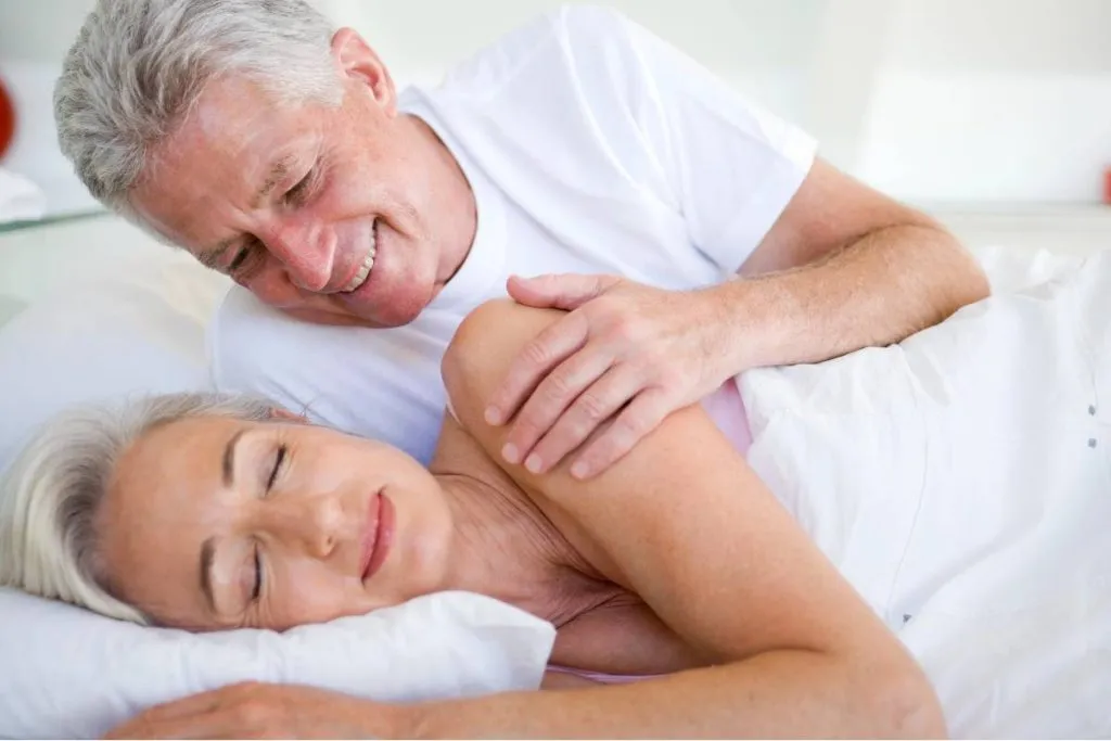 Imagem mostra um casal deitado em uma cama.