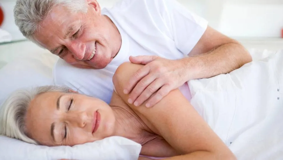 Imagem mostra um casal deitado em uma cama.