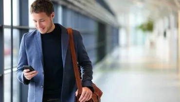 Imagem mostra um homem bem vestido digitando no celular andando em um grande corredor.