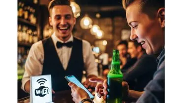 Imagem mostra uma pessoa em um bar utilizando o celular e com uma garrafa de bebida na mão.