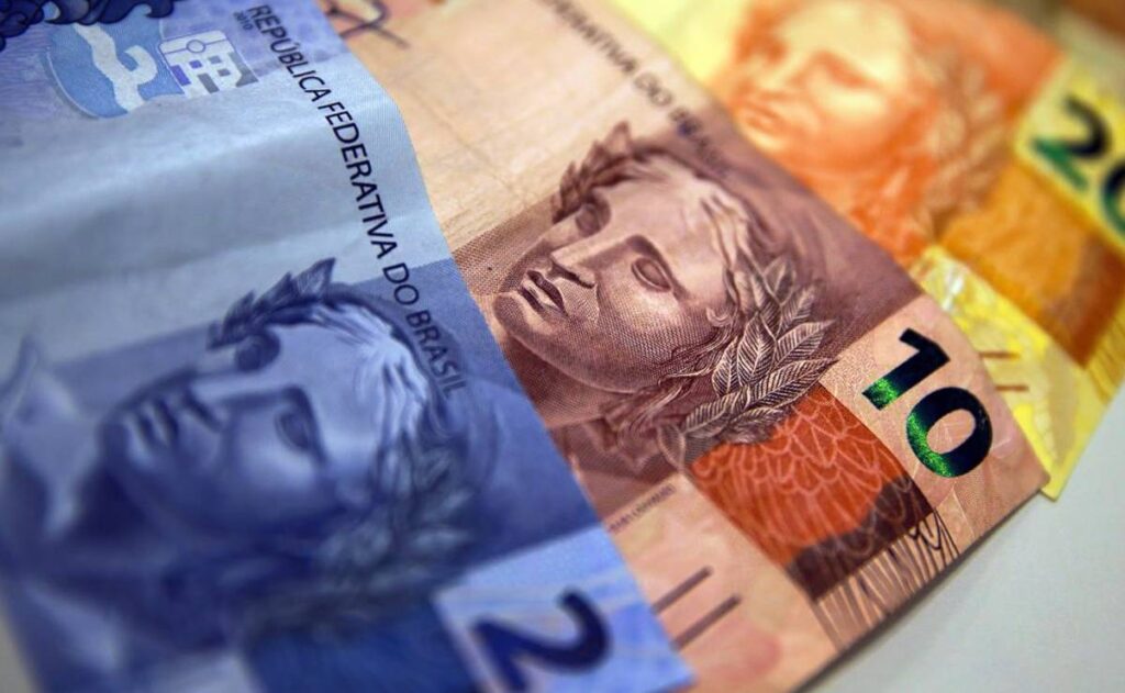 cedulas de real dispostas em uma mesa como um leque. Tem nota de 2, 10 e 20 reais.