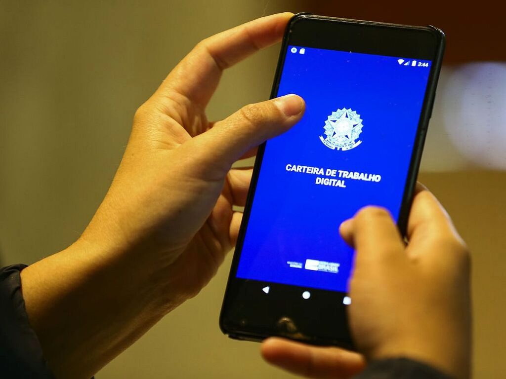Foto mostra uma mão segurando uma carteira digital de trabalho no celular
