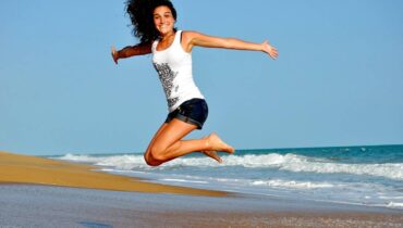 Mulher pula e abre os braços em uma praia