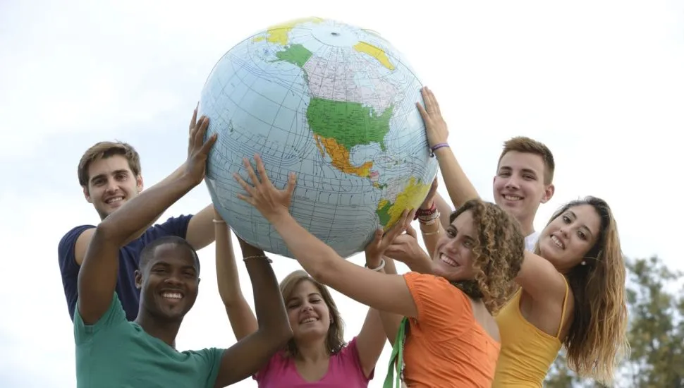 Imagem mostra seis jovens, três homens e três mulheres, cada um com a camiseta de uma cor, Segurando uma esfera que simboliza o globo terrestre