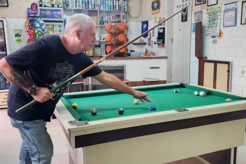 Imagem mostra um homem jogando sinuca em uma mesa clássica