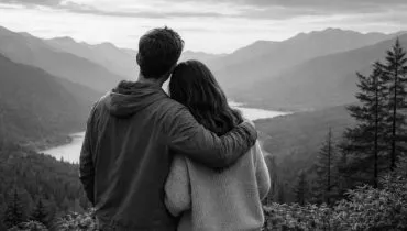 Imagem mostra um casal de costas, em preto e branco, olhando para uma floresta com montanhas ao fundo